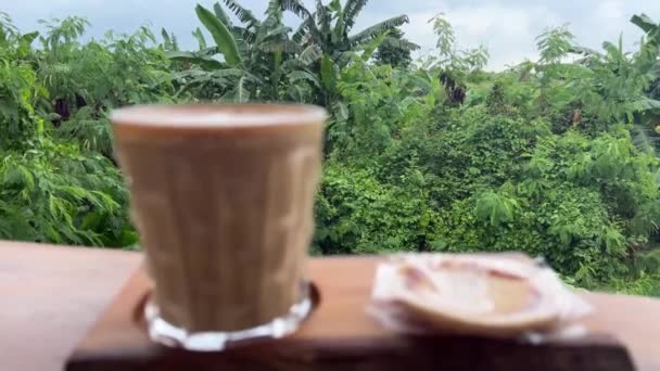 Latte kaffe med kokos kaka mot regnskog — Stockvideo