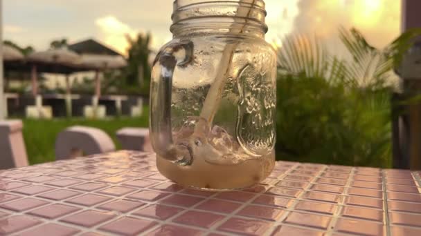 Es teh dalam botol kaca saat matahari terbenam pada ubin merah muda — Stok Video