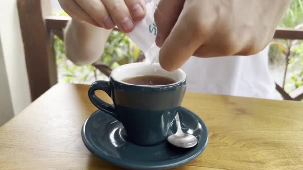 Manos masculinas poniendo azúcar en la taza azul de té negro — Vídeos de Stock