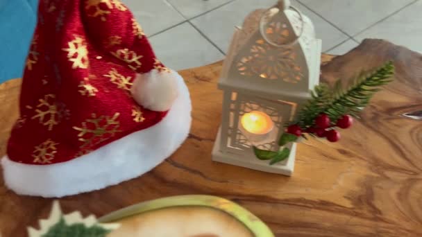 Red Santa klobouk se zlatými sněhovými vločkami, hořící svíčka uvnitř lucerny, kokos s vánoční výzdobou. — Stock video