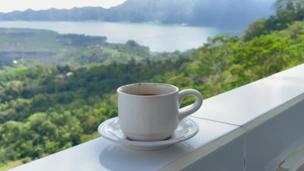 Läckert varmt kaffe på gränsen till terrass med utsikt över bergen i Kintamani Bali. Perfekt morgon med varm dryck med utsikt över berg och sjö med gröna träd. — Stockvideo