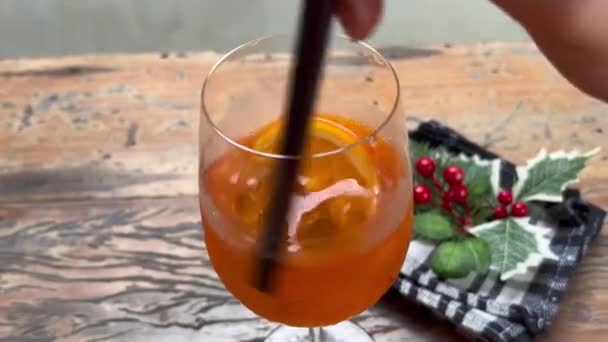 Aperol Spritz Cocktail an Heiligabend umrühren. Genießen Sie die festliche Atmosphäre des Dezembers. Köstliches alkoholisches Getränk im Winter — Stockvideo
