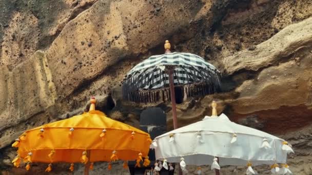 Balinese temple umbrellas color white yellow and black and white. Beautiful parasol near rock in wild nature. — Stock Video
