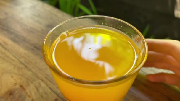 Θηλυκό χέρι ανακατεύοντας χυμό πορτοκαλιού σε ένα ποτήρι με αντανάκλαση των δέντρων και μπλε ουρανό — Αρχείο Βίντεο