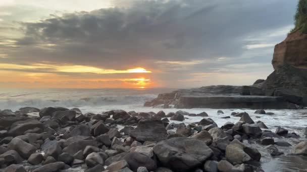 Vacker solnedgång på Bali ön vid havet stranden. Gyllene timmen vid havet med vågor som faller på klipporna. — Stockvideo