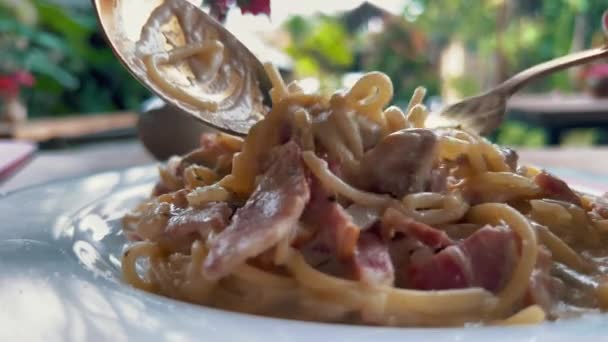 Στρίβοντας μακαρόνια καρμπονάρα σε πιρούνι σε ένα καφέ έξω. Νόστιμα ιταλικά ζυμαρικά με κρεμώδη σάλτσα ζαμπόν. — Αρχείο Βίντεο