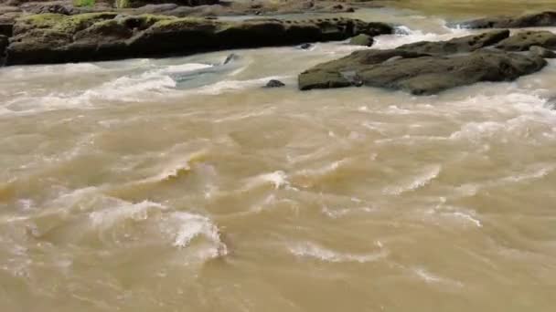 Hnědá voda řeky se sopečným útesem se zeleným mechem. — Stock video