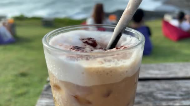 Delizioso caffè al latte freddo in riva al mare in estate. Bevanda fredda al bar sulla spiaggia all'aperto. Viaggiare e godersi l'isola di Bali. — Video Stock