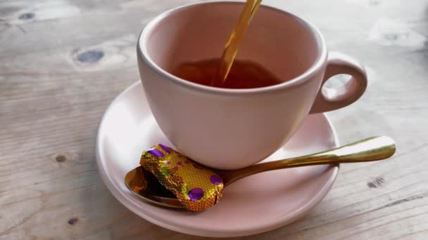 Derramando chá preto quente em uma caneca rosa. Chocolate de coelho de Páscoa em folha de ouro em um pires no momento do chá. Desfrute de bebida quente em um dia de primavera. — Vídeo de Stock