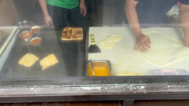 Cuising caffè chef indiano colpendo pezzo di pasta e piegando marmellata di banane dolci. Il processo di clooking roti pane canai attraverso un vetro della finestra. — Video Stock