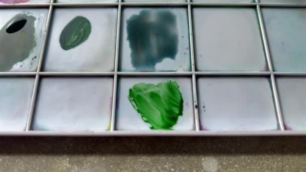 Ανάμιξη πράσινου και κόκκινου για τη γήινη απόχρωση του χρώματος. Καστανά πράσινα σε μια πλαστική παλέτα για ζωγραφική. Καλλιτέχνες χέρι ανάμειξη χρωμάτων με πινέλο. — Αρχείο Βίντεο