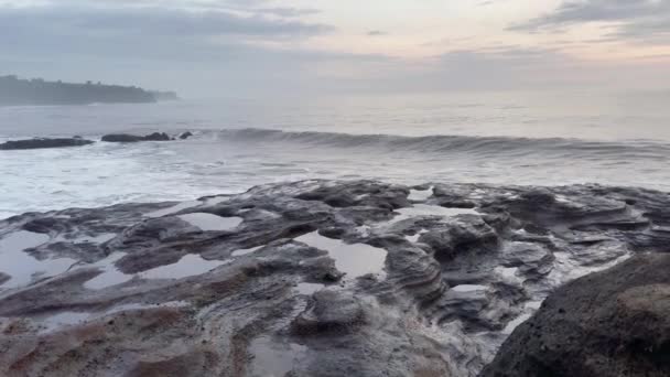 Όμορφη ειρηνική ακτή του ωκεανού μετά το ηλιοβασίλεμα. Γκρι κύματα της θάλασσας συντρίβονται στα μαύρα βράχια στο νησί Μπαλί Balian περιοχή. — Αρχείο Βίντεο