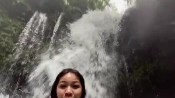 Живая камера с красивой девушкой, плавающей в реке под водопадом. Счастливая женщина смеется, прыгая в водопад в тропических джунглях. — стоковое видео