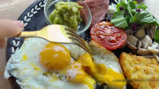 Простой домашний завтрак с яйцами и овощами на солнечной стороне. Жареные яйца и авокадо с авокадо на тарелке с беконом и помидорами на гриле. Голодный человек ест пищу. — стоковое видео