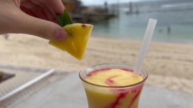 Plaj barında bir bardak tropikal meyve kokteylinden bir parça ananas alan kadın görüntüsü. Deniz kıyısındaki tatlı ve sağlıklı içeceğin tadını çıkar..