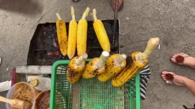 İsimsiz bir şefin, bir tramvayda ızgara mısır pişirişinin en üst görüntüsü. Bir adam kumsalda yelpaze sallayarak mısırın etrafında dönüyor..