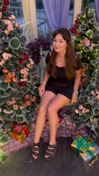 Ein nettes Mädchen sitzt an einem schönen Weihnachtsbaum im traditionellen Vintage-Retro-Stil an einem schönen Ort. Lebensstil der Silvesterfeier. — Stockvideo