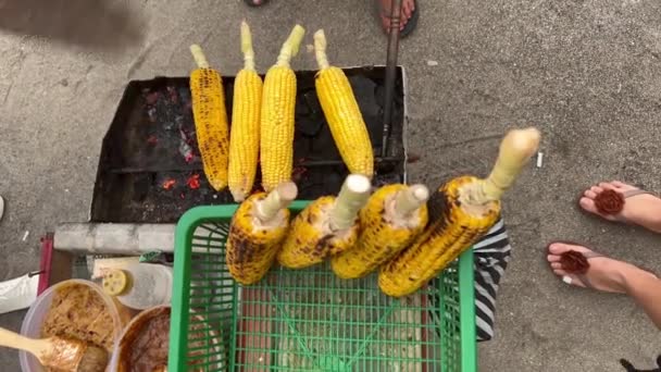 Top view of anonymous chef cooking grilled corn on a trolley. Man turning around corn on a grill waving a fan on a beach. — Stock Video