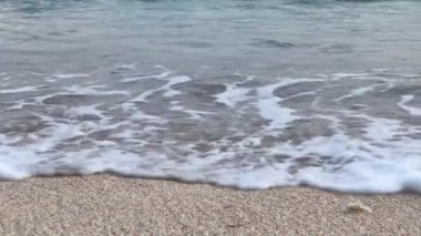 Okyanus dalgalarının beyaz köpüklü suya dönüşüp kumu yıkadığı yakın çekim görüntüsü..