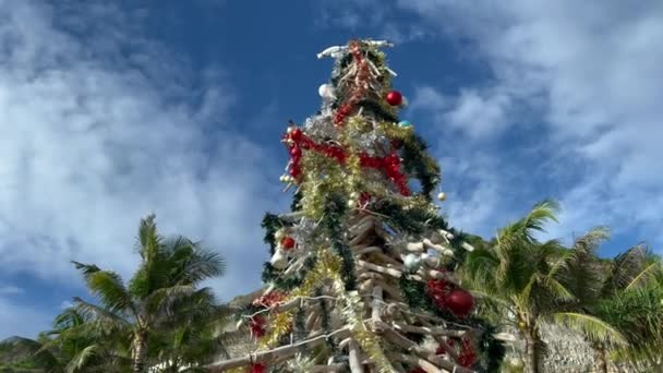 Bellissimo filmato in diretta dell'albero di Natale rosso e dorato realizzato con bastoncini di legno nel paradiso tropicale. Arredo natalizio in località turistica a Bali Melasti spiaggia — Video Stock