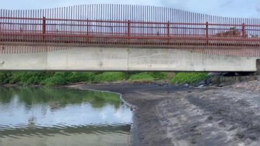 Metal raylı beton bir köprü. Nehir boyunca uzanan siyah kumlu bir nehir. Tropikal cennette palmiye ağaçları ve yeşil kalınlıkta. Tropiklerde Asya doğası.