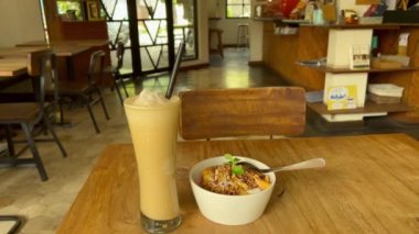 POV meyve ve granola smoothie kasesi yiyor ve sıcak bir kafeteryada buzlu frappe kahve içmeyi bekliyor.