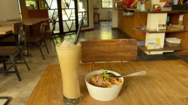 POV eating fruits and granola smoothie bowl and anticipating icy frappe coffee drink inside a cozy caffeteria — Stock Video