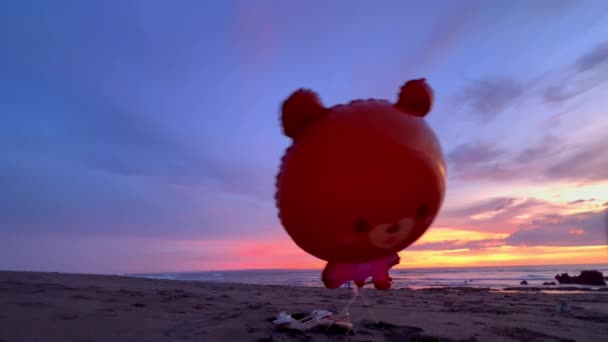 Bonito globo de oso volando sobre la playa de arena al atardecer. Fondo de infancia feliz. — Vídeos de Stock