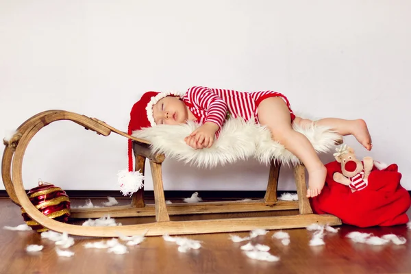 小さな男の子は、サンタの服を着て、そりで寝ています。 — ストック写真