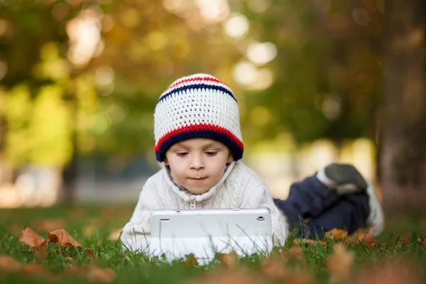 Junge spielt auf dem Tablet auf dem Rasen — Stockfoto