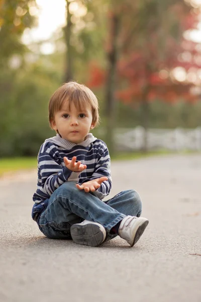 Хлопчик, сидить на шляху в парку — стокове фото