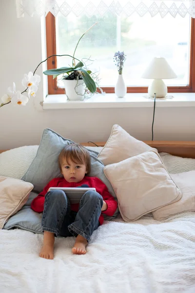 Мальчик, лежа на кровати, играя с планшетом — стоковое фото
