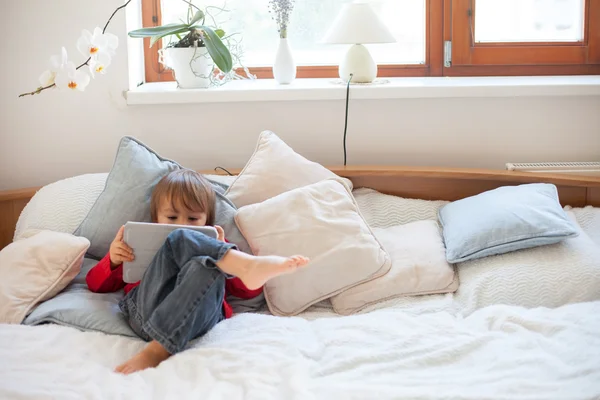 Rapaz, deitado na cama da cama, a brincar com o tablet — Fotografia de Stock