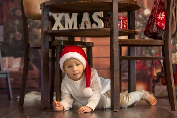 かわいい幼児の子供 クリスマスの男の子 サンタクロースへの手紙を書いて家でクッキーを食べる 居心地の良い木製のコテージ — ストック写真