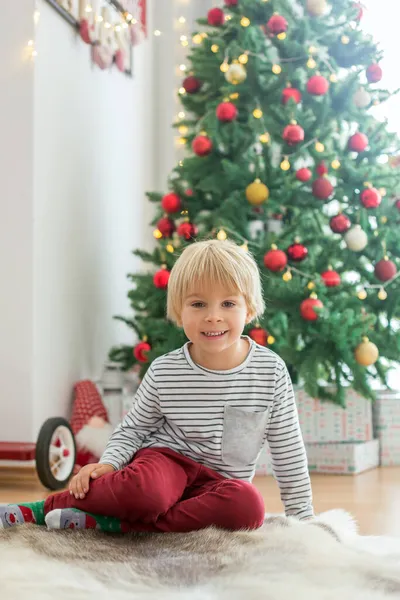 美しい幼児の子供は クリスマスツリーの前に座って 装飾し 彼の周りに提示します — ストック写真