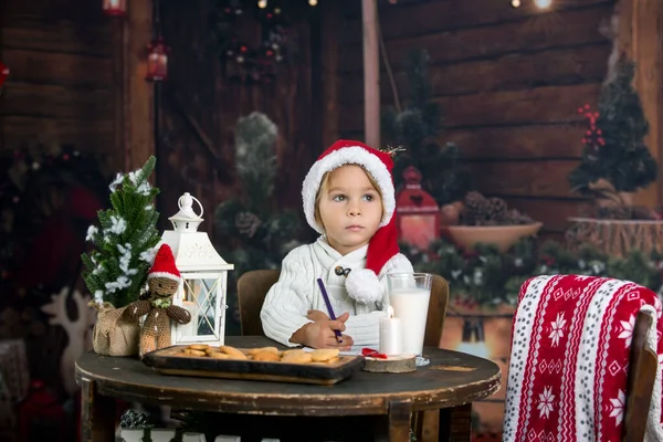 美しい幼児の子供 ブロンドの男の子 サンタクロースへの手紙を書くと自宅でクッキーを食べる クリスマスに居心地の良い雰囲気 — ストック写真