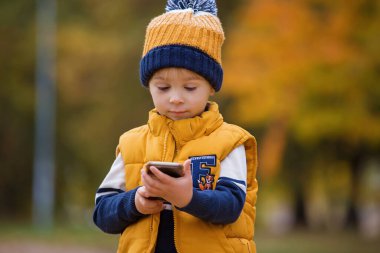 Mutlu çocuk, parkta telefonla oynuyor, annesini arıyor, parkta sonbahar fotoğrafları çekiyor,