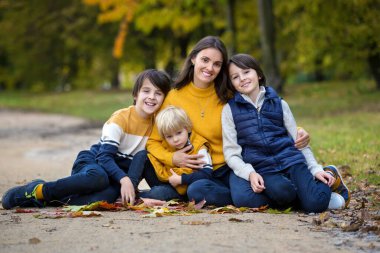 Mutlu bir aile, çocuklu bir anne, sonbahar resimleri parkta çekiliyor, çocuklar oyun oynuyor.