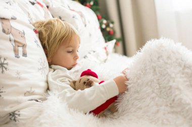 Güzel sarışın çocuk, ateşi olan hasta çocuk, Noel 'de yatakta yatıyor, öksürüyor ve burnu akıyor.