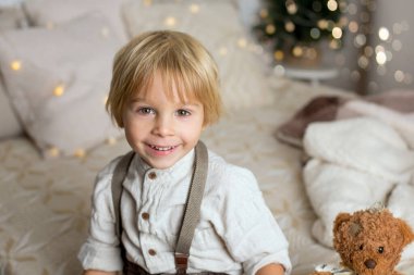 Çocuk yatakta oturuyor, boho stili, gülümsüyor, şık giyimli şirin bir çocuk.