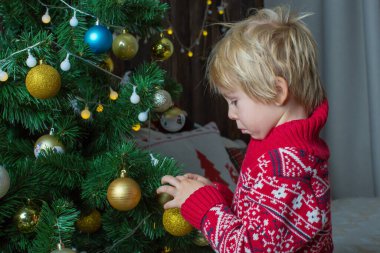 Küçük tatlı bir çocuk, noel kıyafetleri içinde bir çocuk, Noel 'de ahşap bir kulübede oynamak, onun etrafında dolaşmak. Çocuk kitabı okuyor ve çay içiyor.