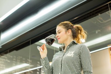 Genç ve çekici bir kadın, şarap dükkanında şarap tadıyor, bir bardak lezzetli kırmızı ya da beyaz şaraptan hoşlanıyor.