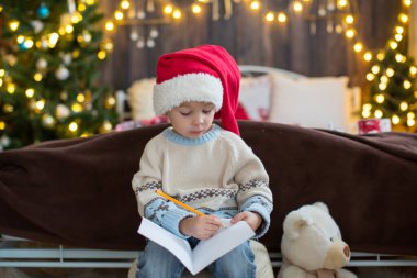 Sevimli bir çocuk, Noel kıyafetli bir çocuk, Noel 'de tahta bir kulübede oynuyor, etrafında süslemeler yapıyor. Çocuk kitabı okuyor ve çay içiyor.