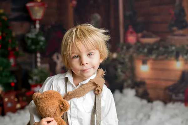 かわいいファッション幼児の男の子 木製のキャビンログ クリスマスの装飾の前にテディベアで雪の中で遊んで — ストック写真