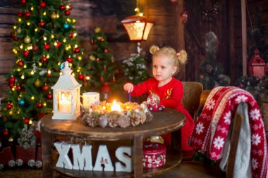 Şirin sarışın çocuk, iki at kuyruklu kıvırcık kız, Noel süslemeli bir masada oturuyor, mektup yazıyor ve Noel oyuncaklarıyla oynuyor.