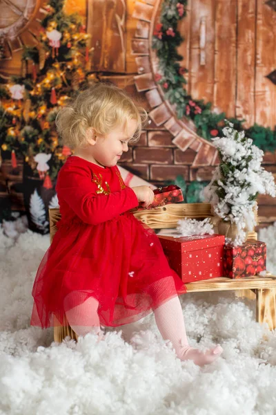 かわいいブロンドの子供 巻き女の子 クリスマスの装飾と木製のキャビンに座って プレゼントを開く 幸せな子供時代 — ストック写真