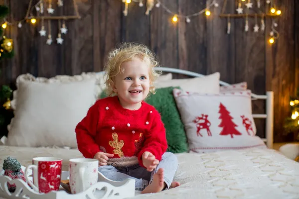 かわいい幼児の子供 クリスマスの服の巻きブロンドの女の子 クリスマスに木製のキャビンで遊んで 彼女の周りの装飾 児童書やお茶を飲む — ストック写真