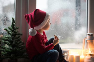 Güzel çocuk, evlat, Noel arifesinde pencerenin önünde Noel Baba 'yı merakla bekliyor.