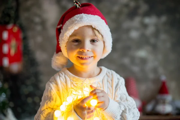 美しい幼児の男の子 クリスマスの光の文字列を保持 カメラを見て 閉じるクリスマスの肖像画 — ストック写真