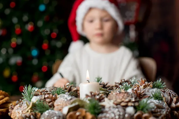 真ん中にロウソクを灯すアドベントリース背景に手紙を書く子供背後にクリスマスツリー — ストック写真
